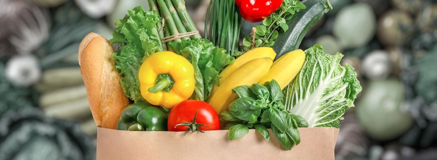 Brown paper grocery bag overstuffed with various vegetables and a stick of bread to denote healthy food choices.