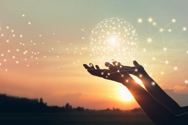 Pair of hands silhouetted against a setting sun hold an illustrated ball of illuminated user icons.