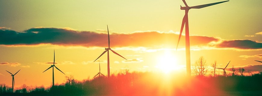 Power-generation windmills on a hilltop silhouetted by the rising or setting sun behind them.